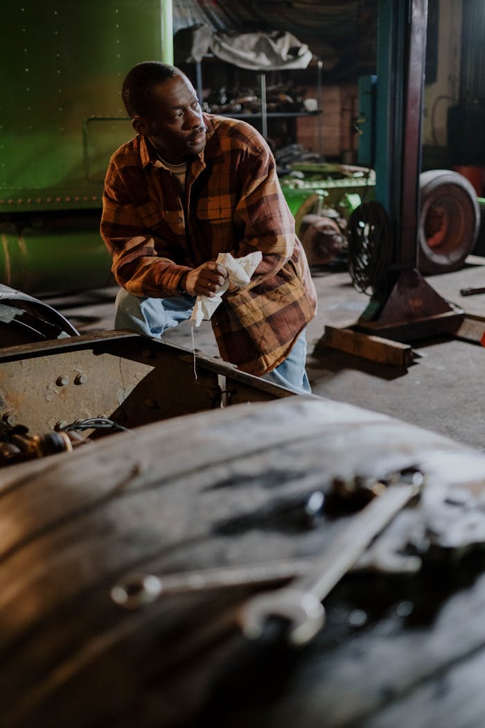 An African American mechanic in a garage workshop holding tools, surrounded by equipment.